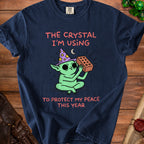 T-shirt graphic: green creature with wizard hat holding brick, text "The crystal I'm using to protect my peace this year."