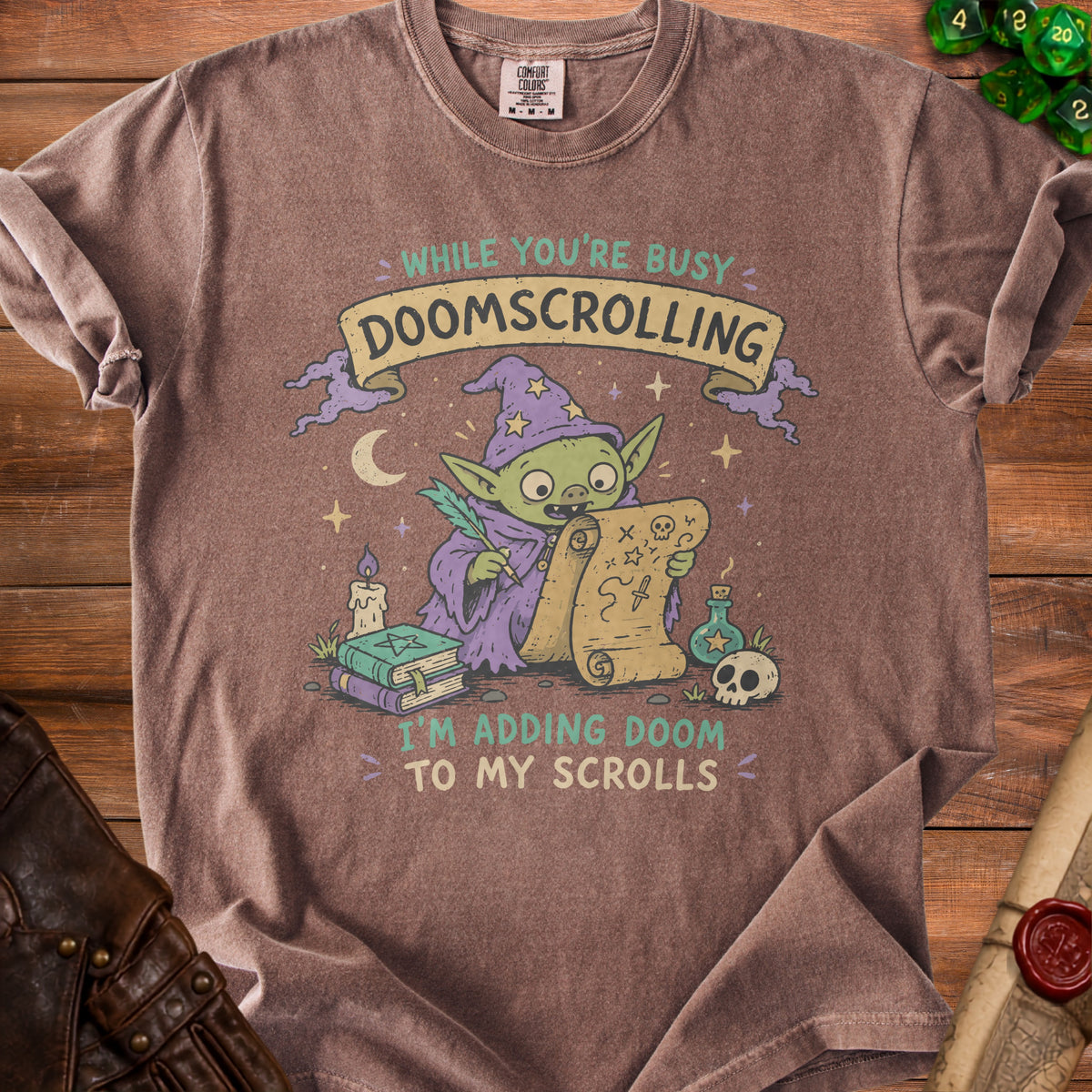 Brown t-shirt with goblin wizard adding doom to scrolls, text says "While you're busy doomscrolling, I'm adding doom to my scrolls."