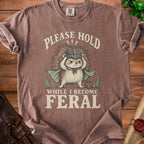 T-shirt with hedgehog wearing helmet and cape, text "PLEASE HOLD WHILE I BECOME FERAL".