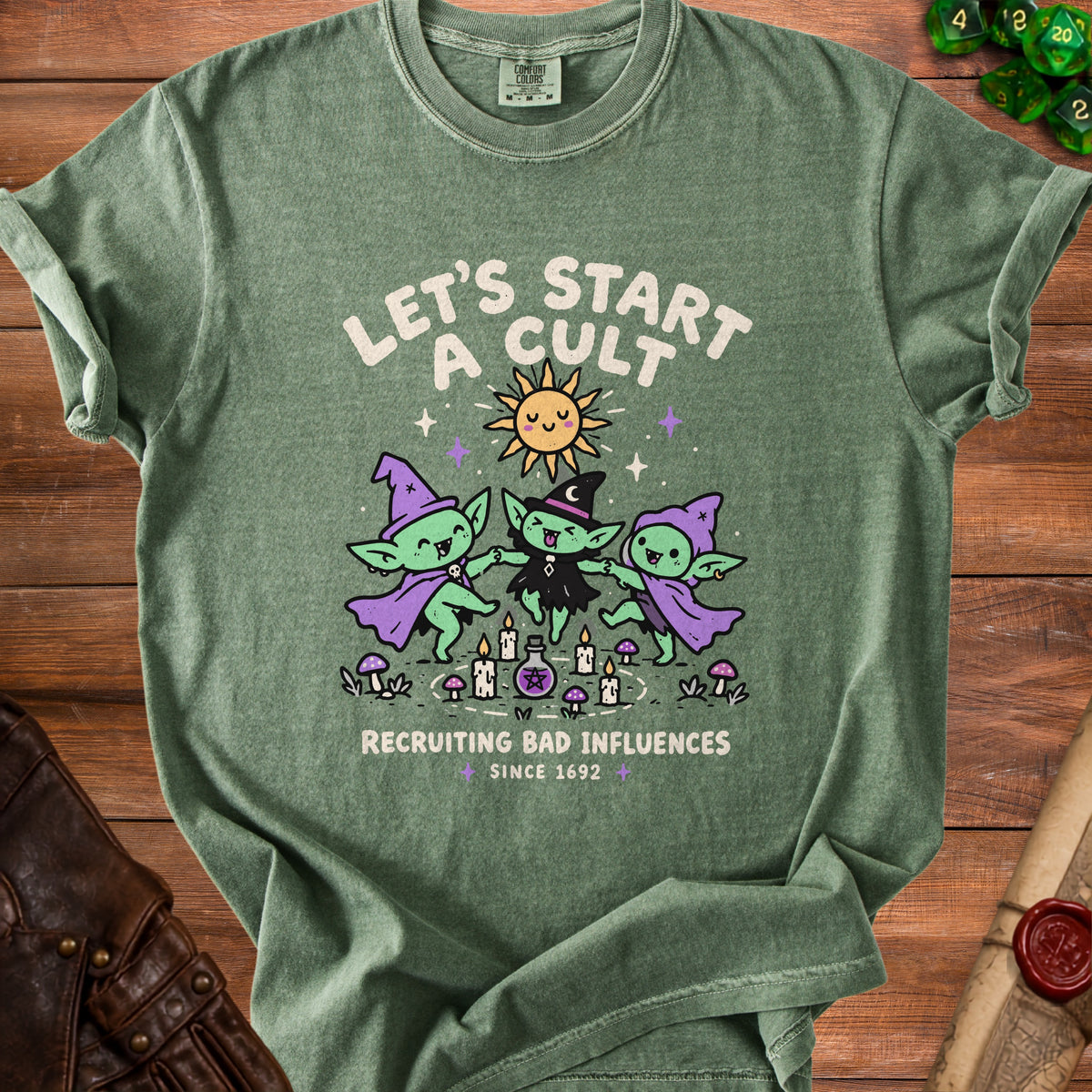 Green t-shirt with cartoon witches, sun, and text "Let's Start A Cult Recruiting Bad Influences".