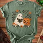 Ghost reading a book next to a pumpkin with floral and mushroom accents.