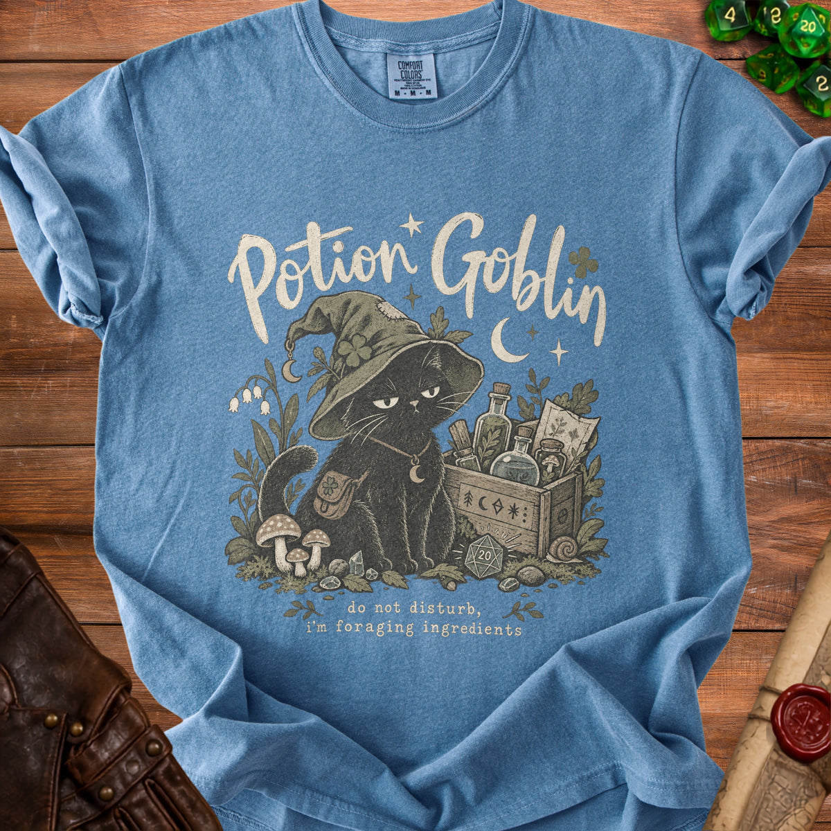 Blue t-shirt featuring a black cat in a witch hat with "Potion Goblin" and "do not disturb, I'm foraging ingredients."