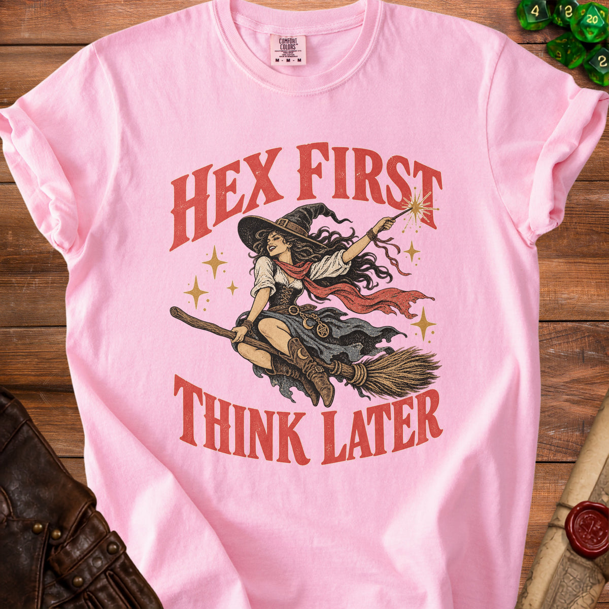 Pink t-shirt featuring a witch riding a broomstick with the text HEX FIRST THINK LATER.