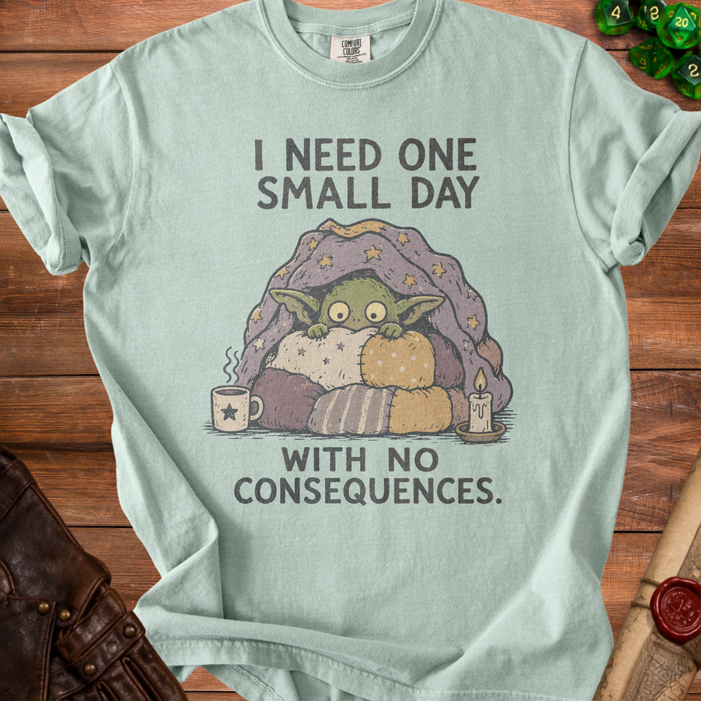 T-shirt with graphic of a creature under a blanket, text: "I need one small day with no consequences."
