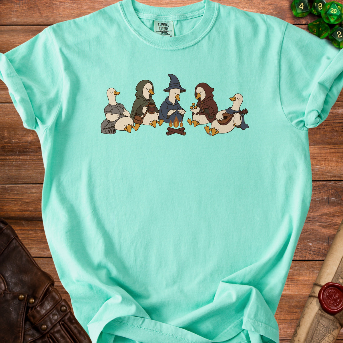 Five ducks in fantasy attire sit around a campfire on a teal t-shirt.