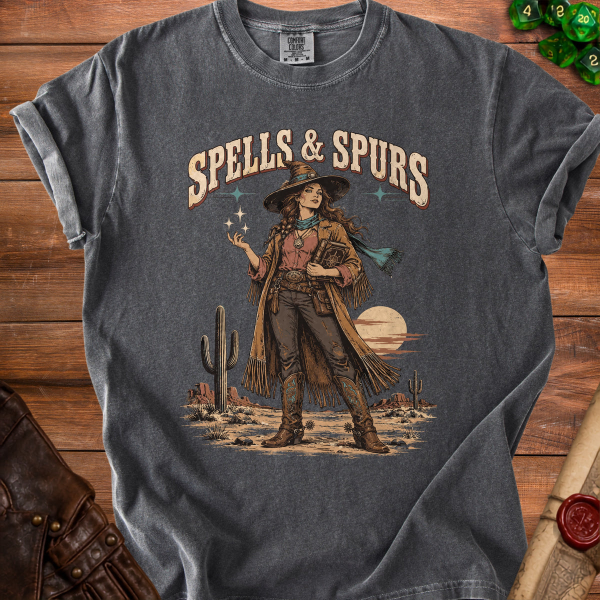 Graphic tee with "Spells & Spurs" text, a witchy cowgirl, and desert landscape.