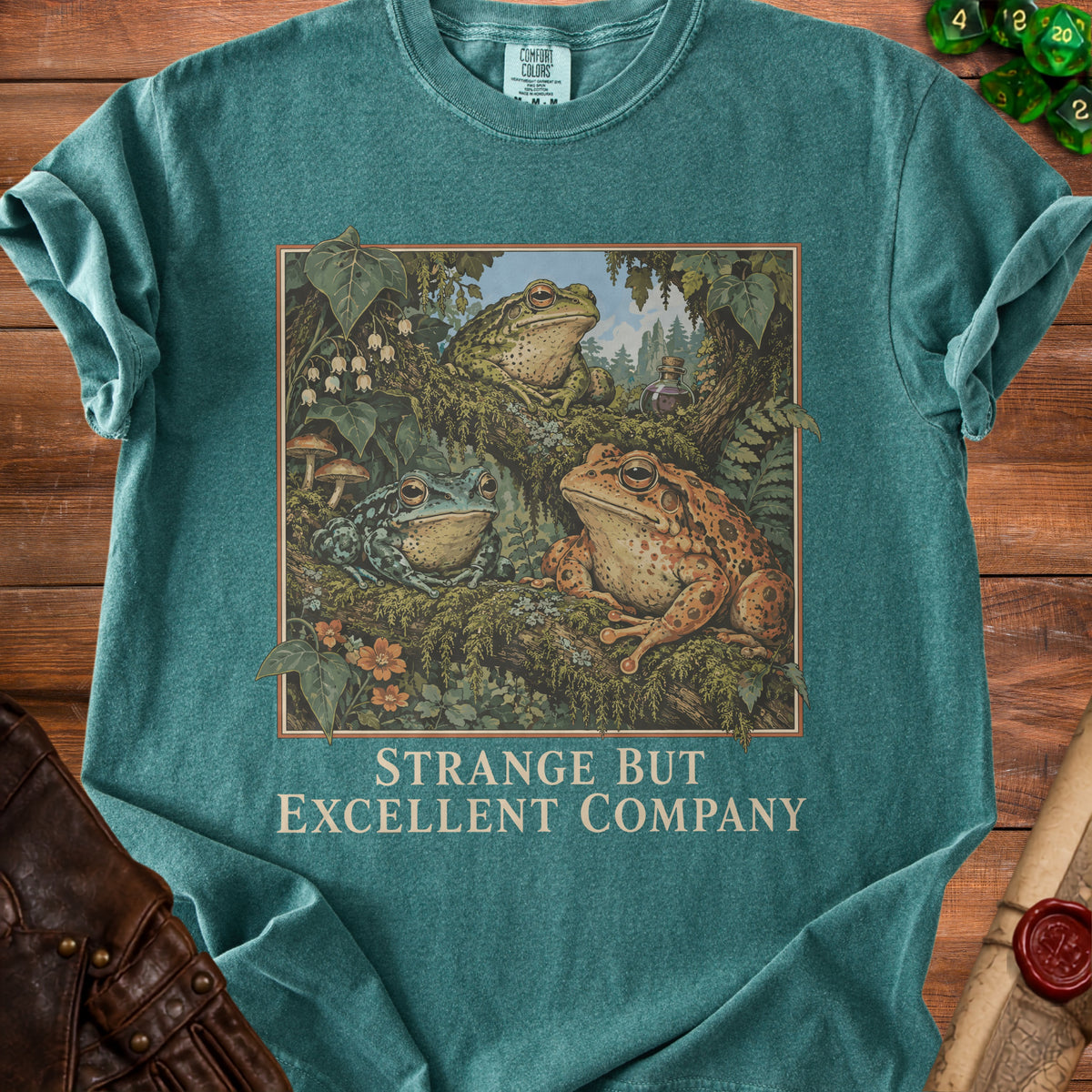 Teal t-shirt with "Strange But Excellent Company" text and a forest scene with three frogs.