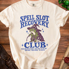 Cream t-shirt with wizard frog design: "Spell Slot Recovery Club" and event details.