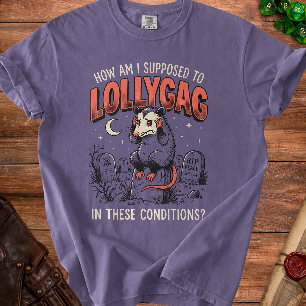 T-shirt graphic of a sad possum in a graveyard saying "How am I supposed to lollygag in these conditions?".