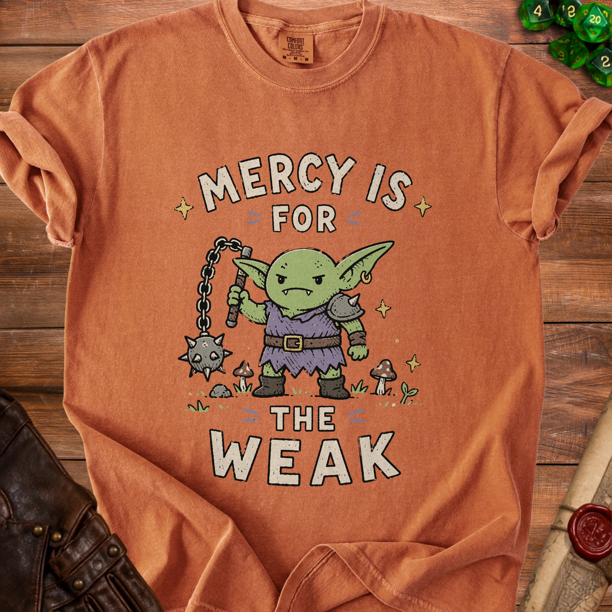 Orange t-shirt with a cartoon goblin holding a flail and the text "Mercy is for the weak".