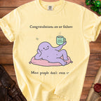 Light yellow t-shirt with cartoon: "Congratulations on ur failure. Good enough. Most people don't even try."