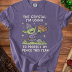 Purple t-shirt graphic with a goblin wizard holding a brick and the text "The crystal I'm using to protect my peace this year".