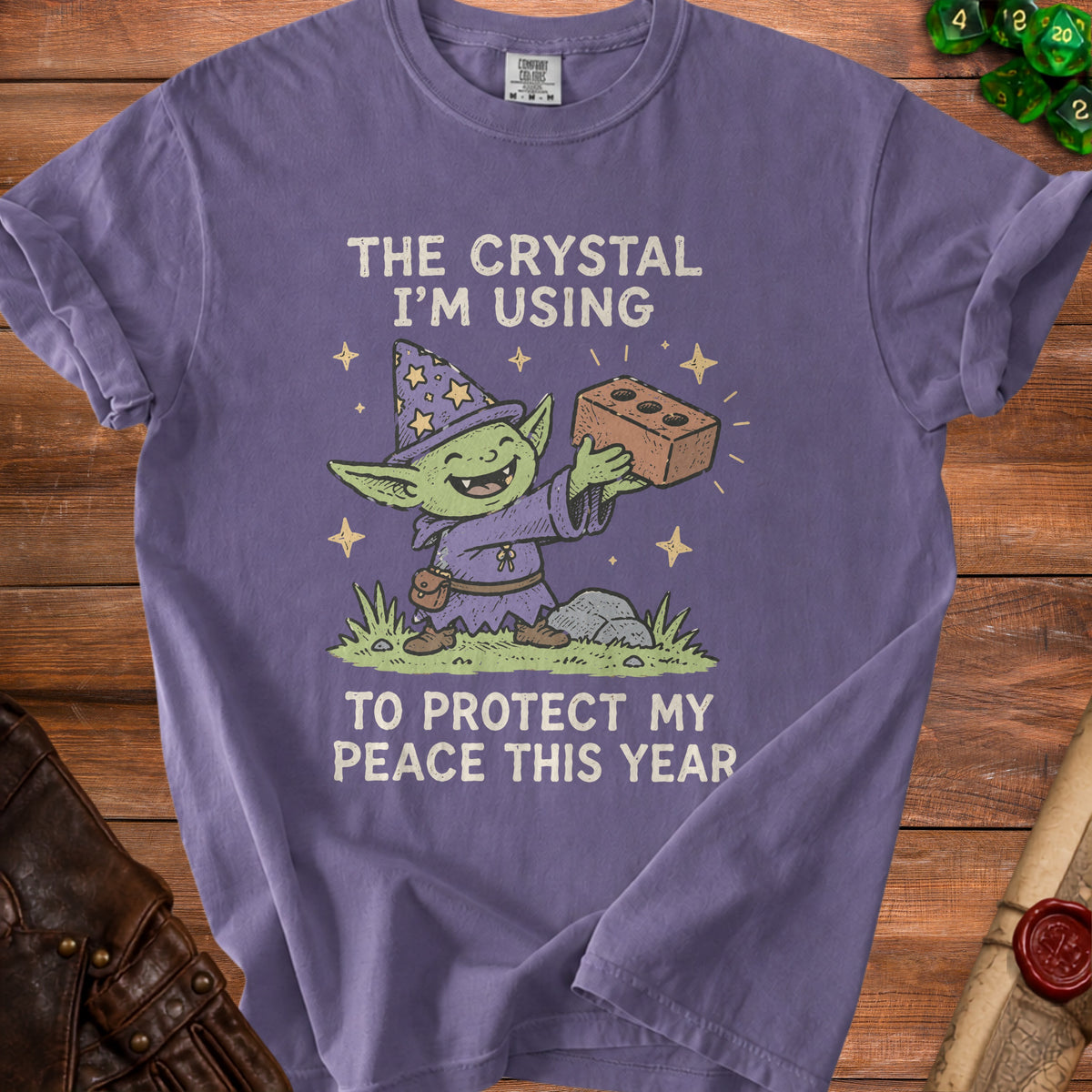 Purple t-shirt graphic with a goblin wizard holding a brick and the text "The crystal I'm using to protect my peace this year".