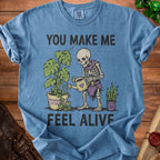 Skeleton watering plants with text "YOU MAKE ME FEEL ALIVE".