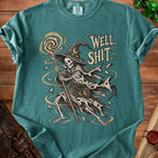 A teal t-shirt featuring a graphic of a skeleton wizard casting a spell with the text Well, Shit...