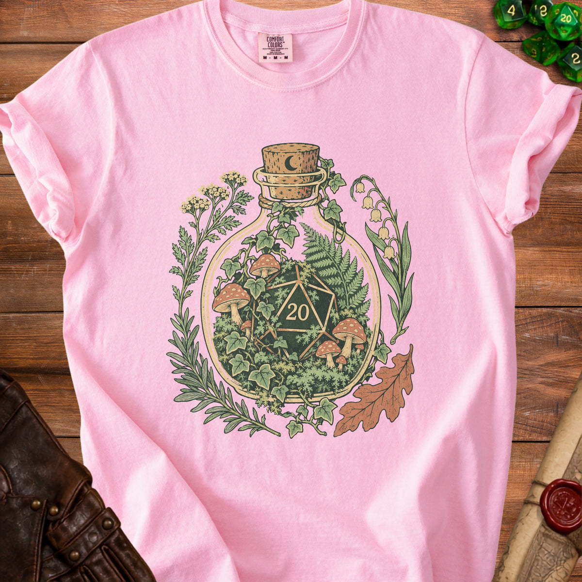 Pink t-shirt with a bottle containing a D20 die and botanical elements.