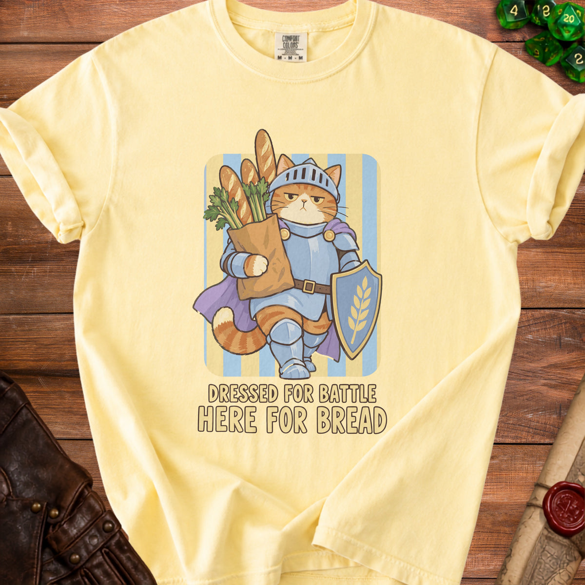 Yellow t-shirt with graphic of cat knight holding bread and greens; text reads "DRESSED FOR BATTLE HERE FOR BREAD."