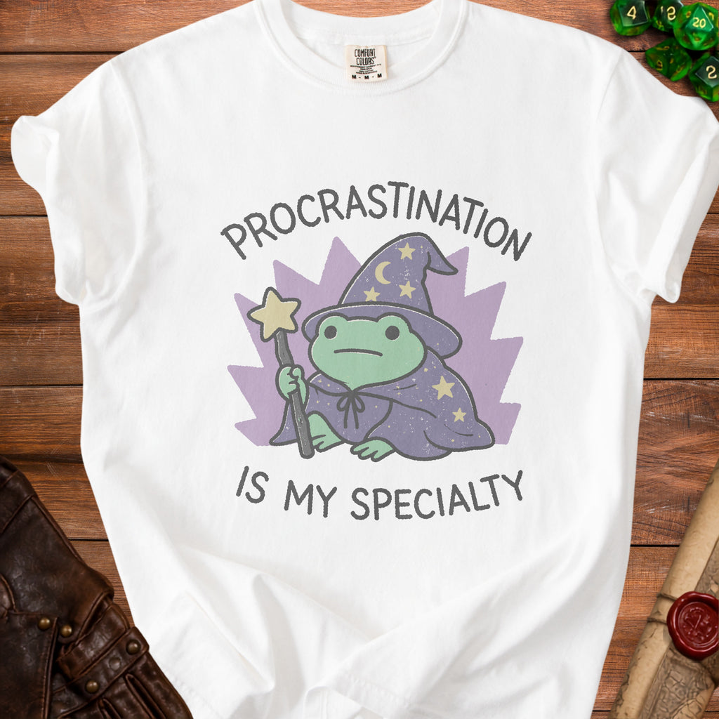 White t-shirt with a frog wizard graphic that says "Procrastination is my specialty".