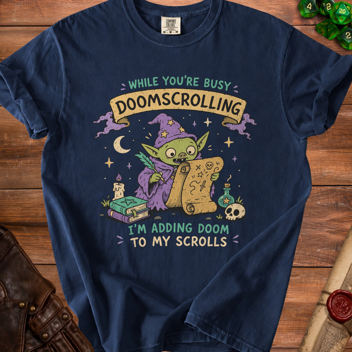 Navy t-shirt with a graphic of a goblin wizard adding doom to scrolls, reading "While you're busy doomscrolling, I'm adding doom to my scrolls."