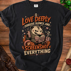 Black t-shirt with possum reading, phone, and coffee, saying "I LOVE DEEPLY FORGIVE SLOWLY, AND SCREENSHOT EVERYTHING".