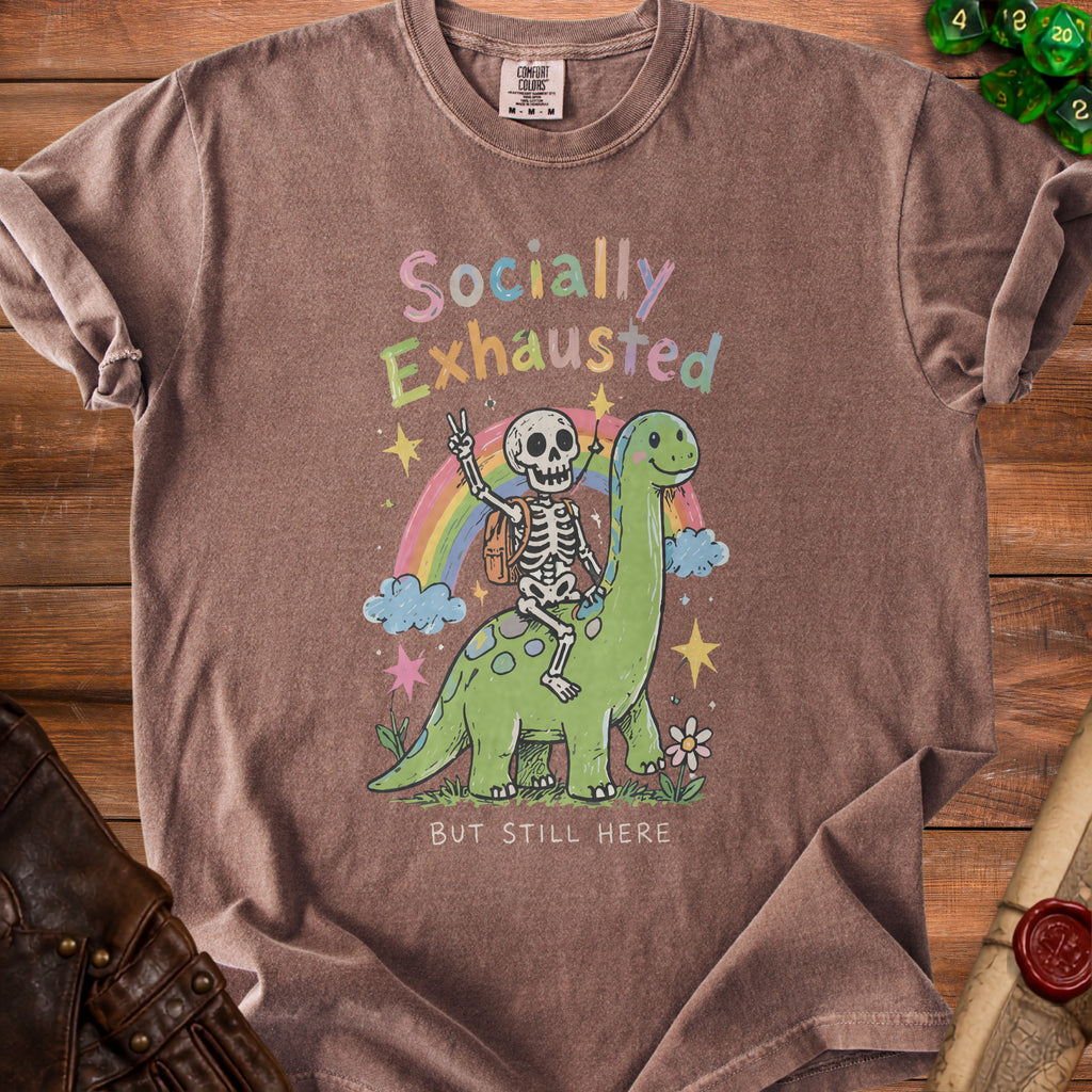 Brown t-shirt graphic of skeleton riding dinosaur, "Socially Exhausted But Still Here."