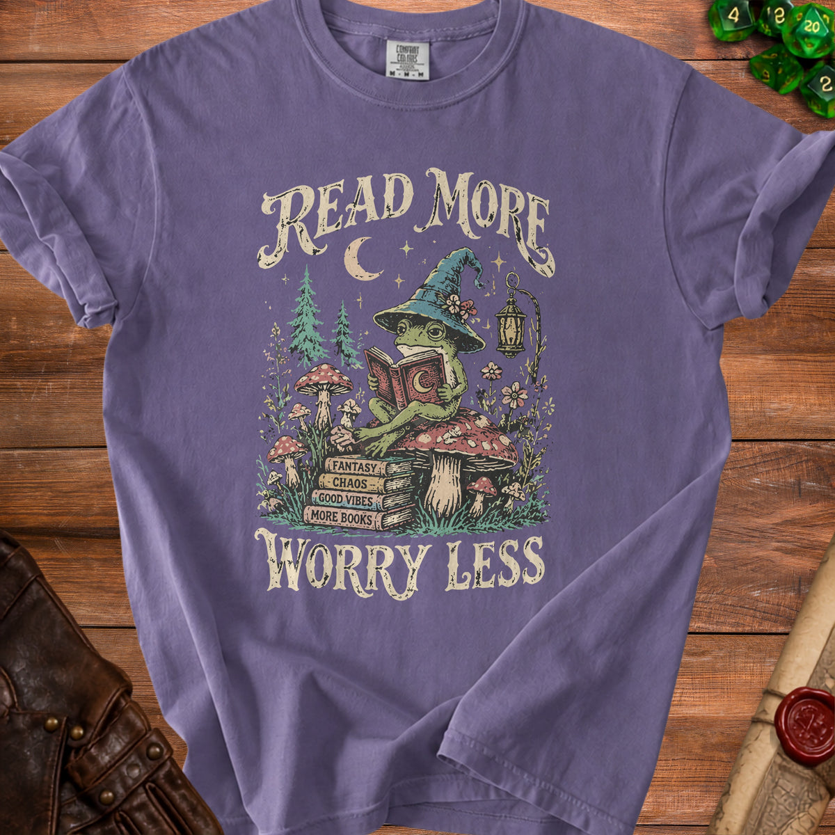 Purple t-shirt with graphic of a frog reading on mushrooms, saying "Read More Worry Less".