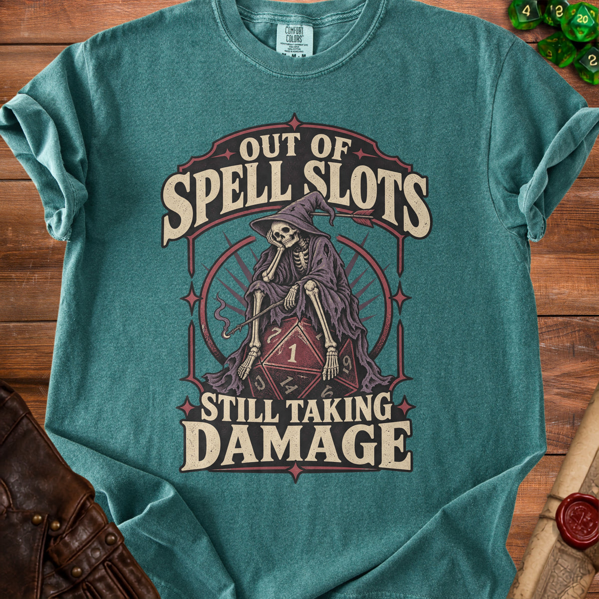 Teal t-shirt with skeleton wearing wizard hat on D20, "Out of Spell Slots Still Taking Damage".