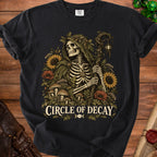 Skeleton in a green hooded cloak surrounded by flowers and text "CIRCLE OF DECAY".