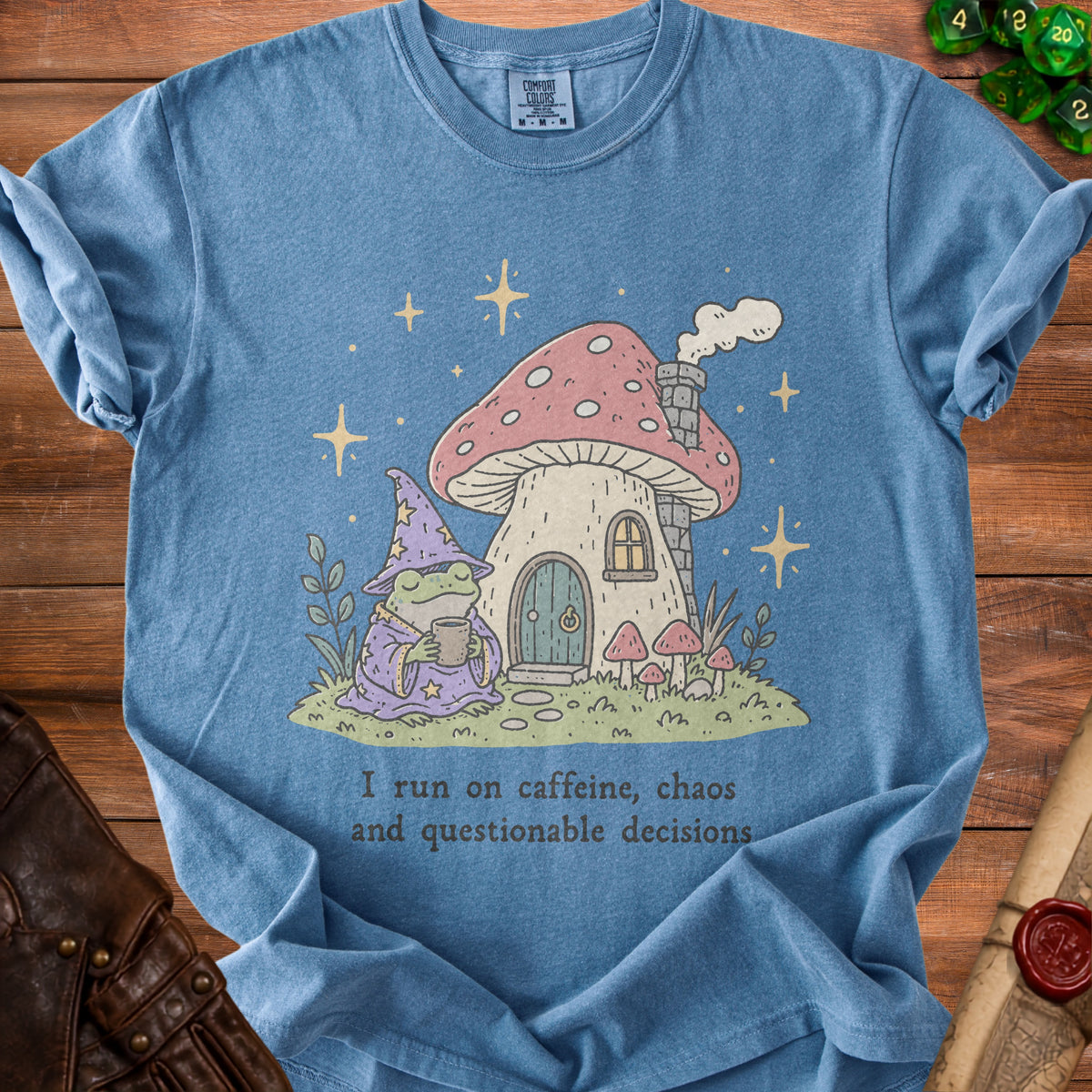 Blue t-shirt with wizard frog holding coffee next to mushroom house, text "I run on caffeine, chaos and questionable decisions".