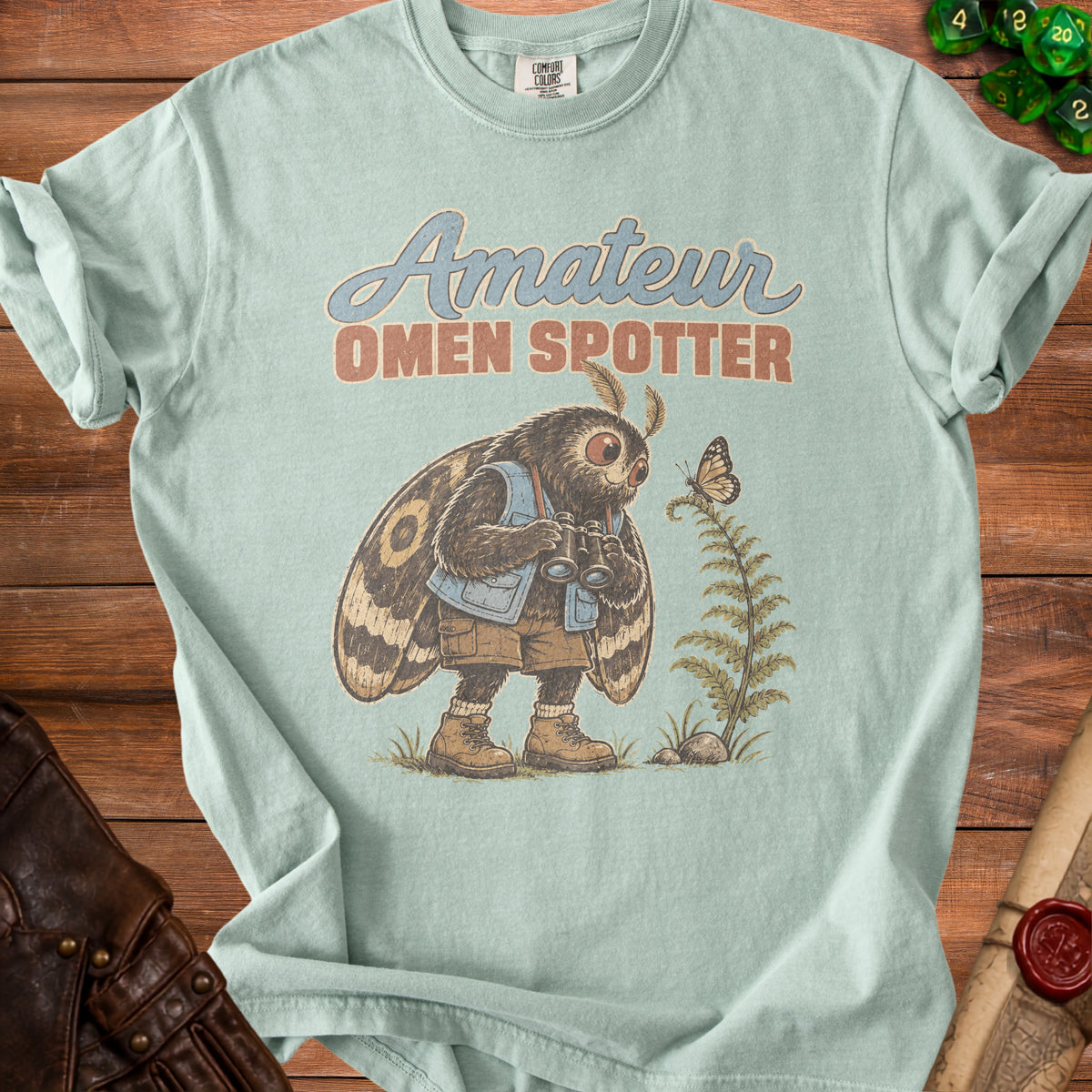 Light blue t-shirt with "Amateur Omen Spotter" text and moth character with binoculars.