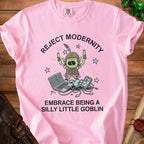 Pink t-shirt with a goblin character breaking a laptop and phone. Text says: "Reject Modernity Embrace Being a Silly Little Goblin".