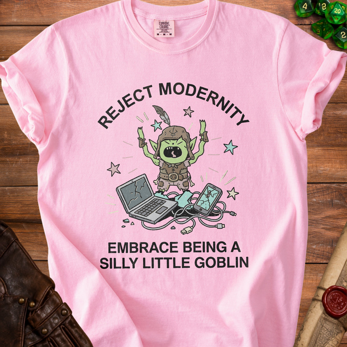 Pink t-shirt with a goblin character breaking a laptop and phone. Text says: "Reject Modernity Embrace Being a Silly Little Goblin".