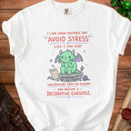 White t-shirt with text: "I love when doctors say 'Avoid Stress' like I can just unsubscribe from the economy and become a decorative gargoyle."