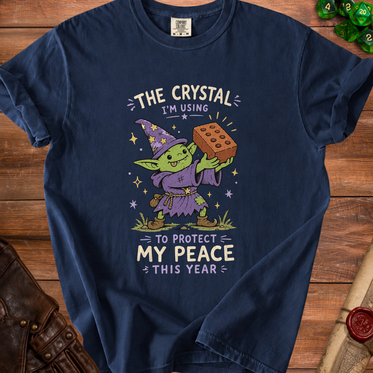 T-shirt graphic of a goblin wizard holding a brick, reading "The crystal I'm using to protect my peace this year".