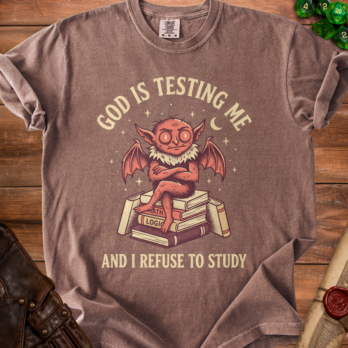 Brown t-shirt with cartoon demon reading books and text "God is testing me and I refuse to study".