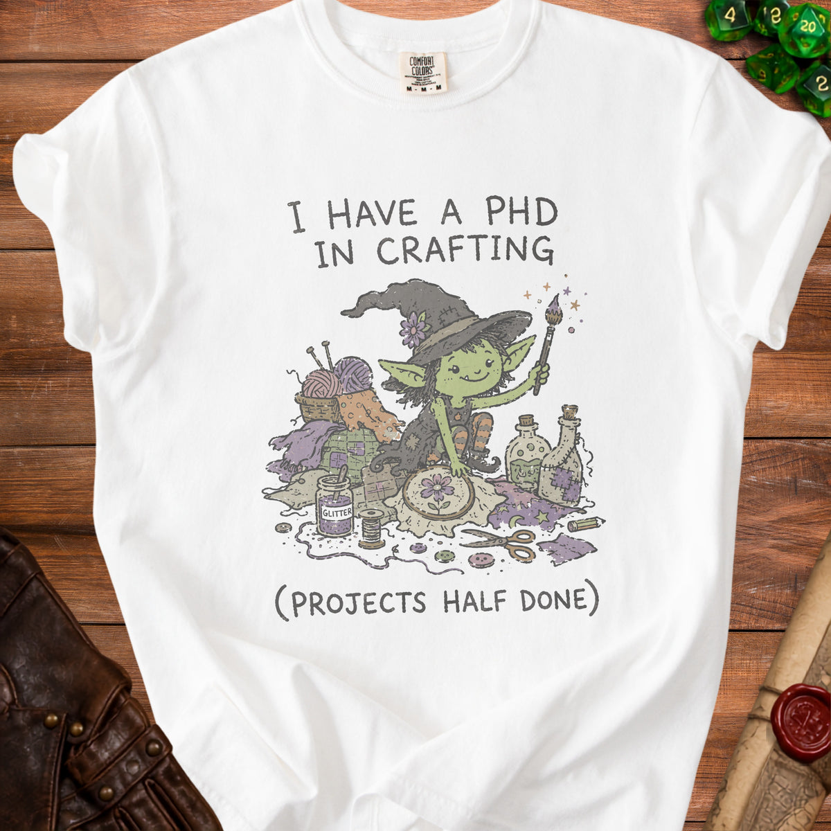 White t-shirt with illustration of a witch surrounded by crafting supplies and text.