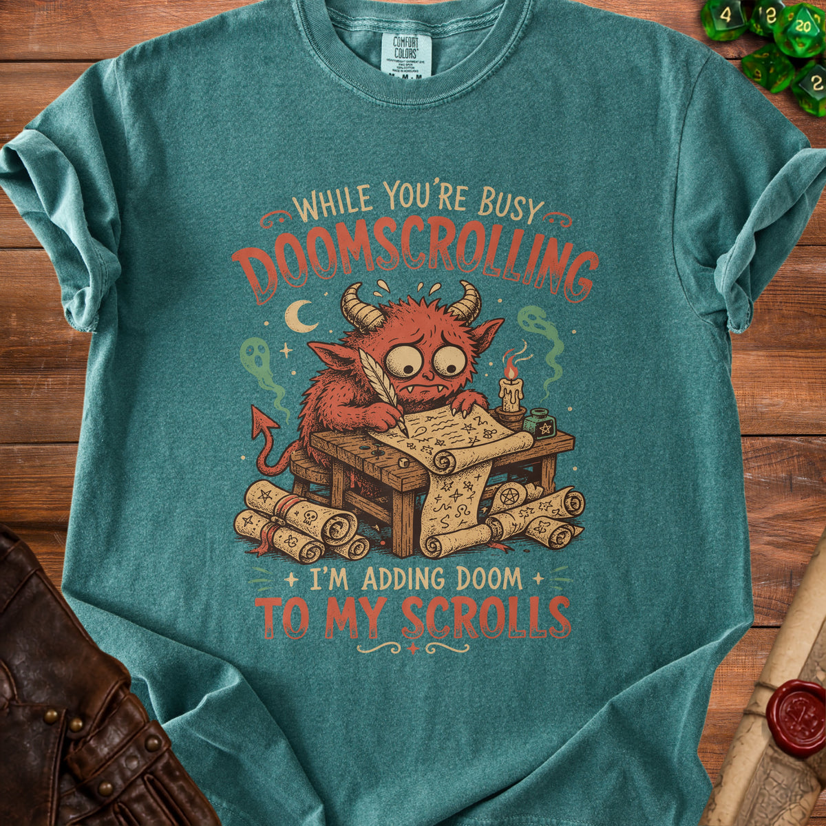 Green t-shirt with a red devil writing on scrolls, reading "While you're busy doomscrolling, I'm adding doom to my scrolls."