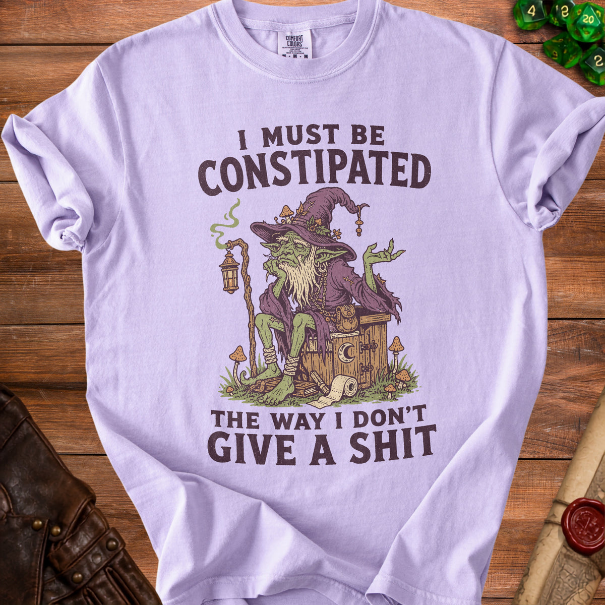 Light purple t-shirt with a goblin graphic and text: "I Must Be Constipated The Way I Don't Give a Shit."
