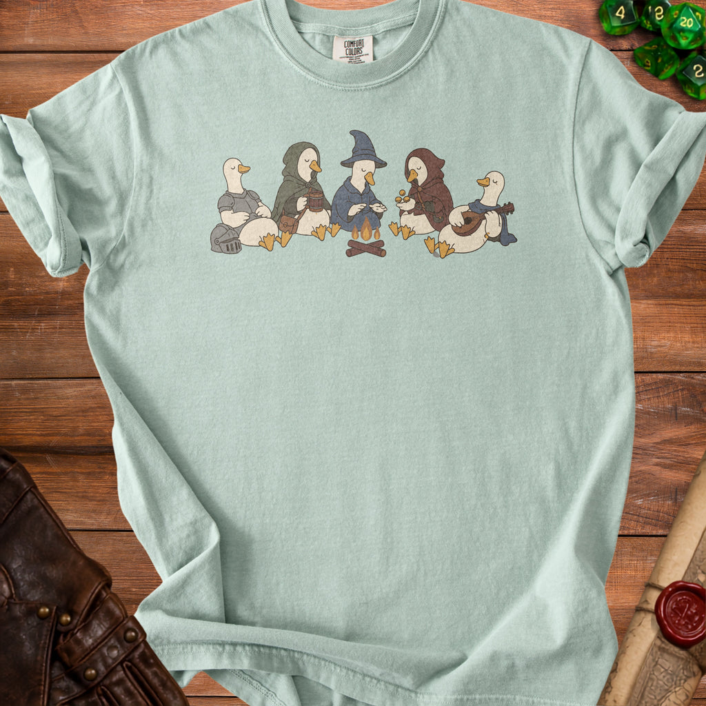 Light blue t-shirt with a graphic of five ducks in fantasy costumes by a campfire.