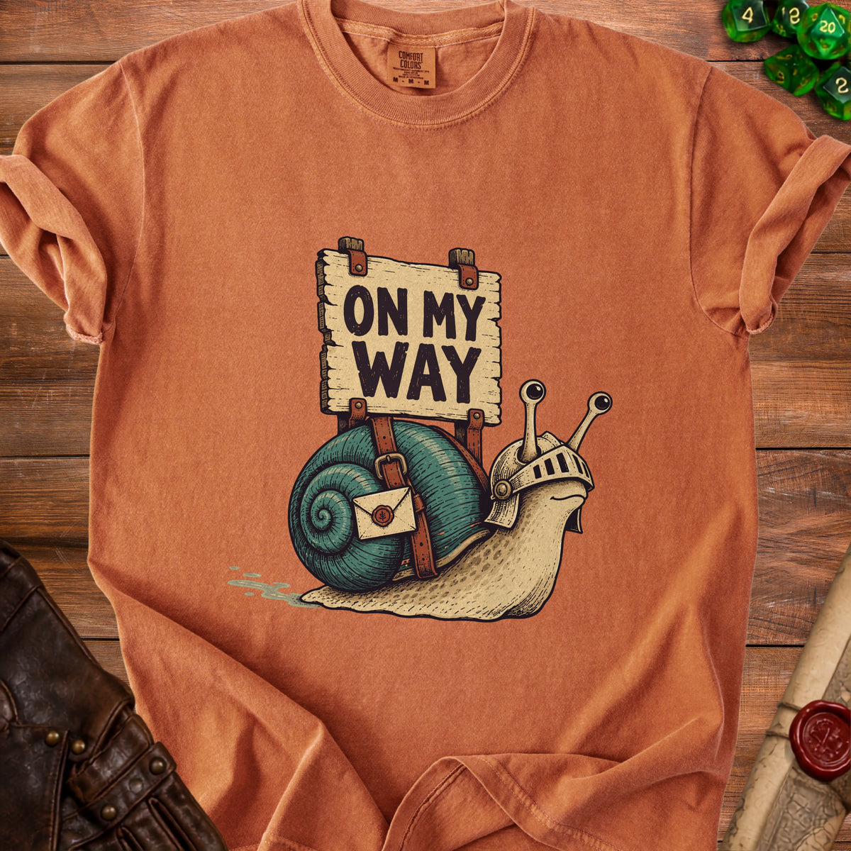 Orange t-shirt with a snail wearing armor and a sign that reads "ON MY WAY."
