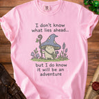 Pink t-shirt with illustration of a mushroom character and text "I don't know what lies ahead... but I do know it will be an adventure".