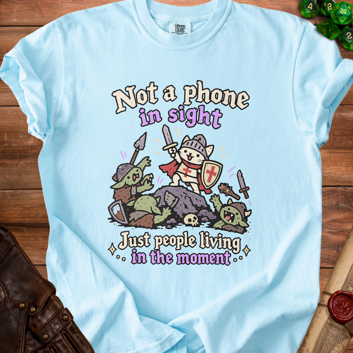 Light blue t-shirt with cartoon cat knight fighting goblins, text "Not a phone in sight".
