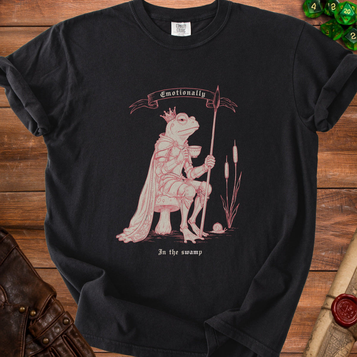 T-shirt graphic of a crowned frog in armor holding a spear and tea, with text "Emotionally In the swamp".