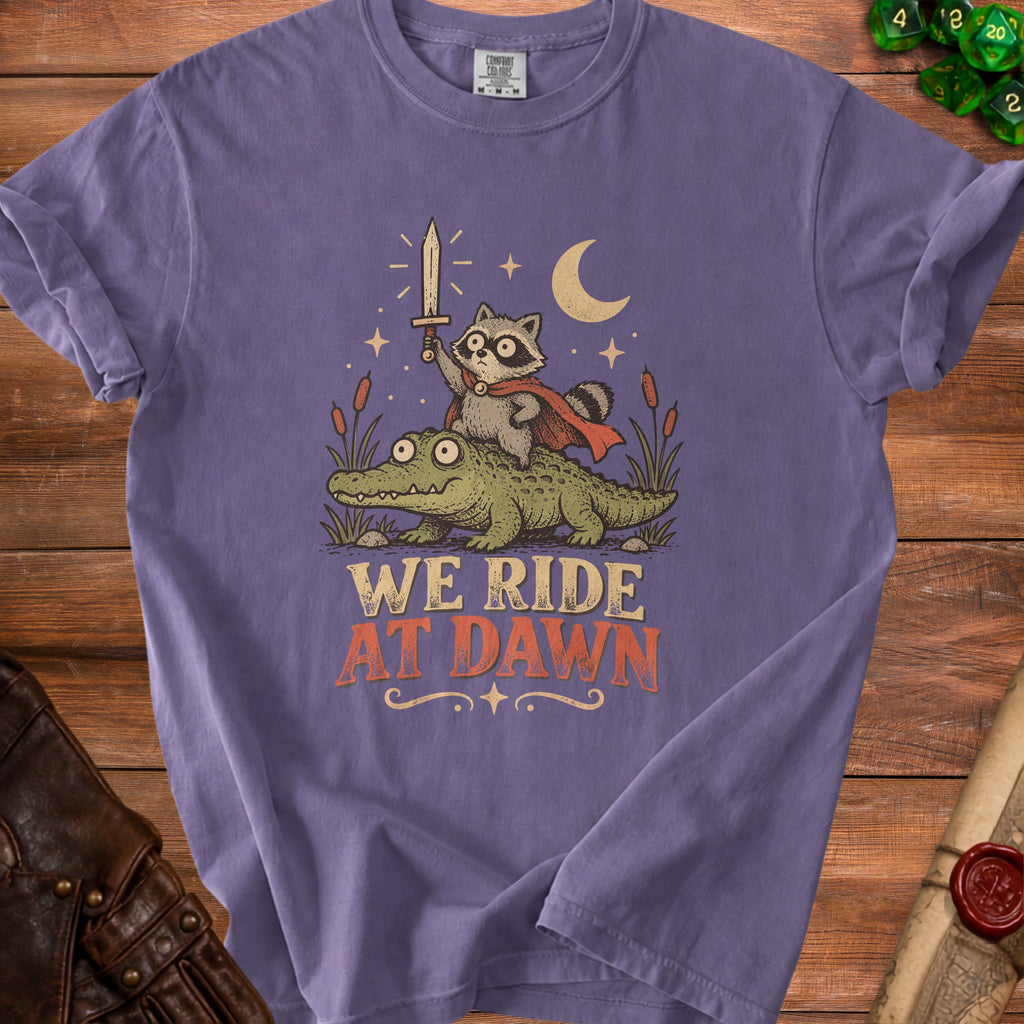T-shirt with raccoon holding sword riding alligator, text "WE RIDE AT DAWN."