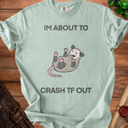 Pale green t-shirt with a graphic of a possum and text: "IM ABOUT TO CRASH TF OUT".