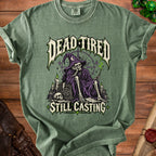Green t-shirt with "Dead Tired Still Casting" graphic of a skeleton wizard with spell items.