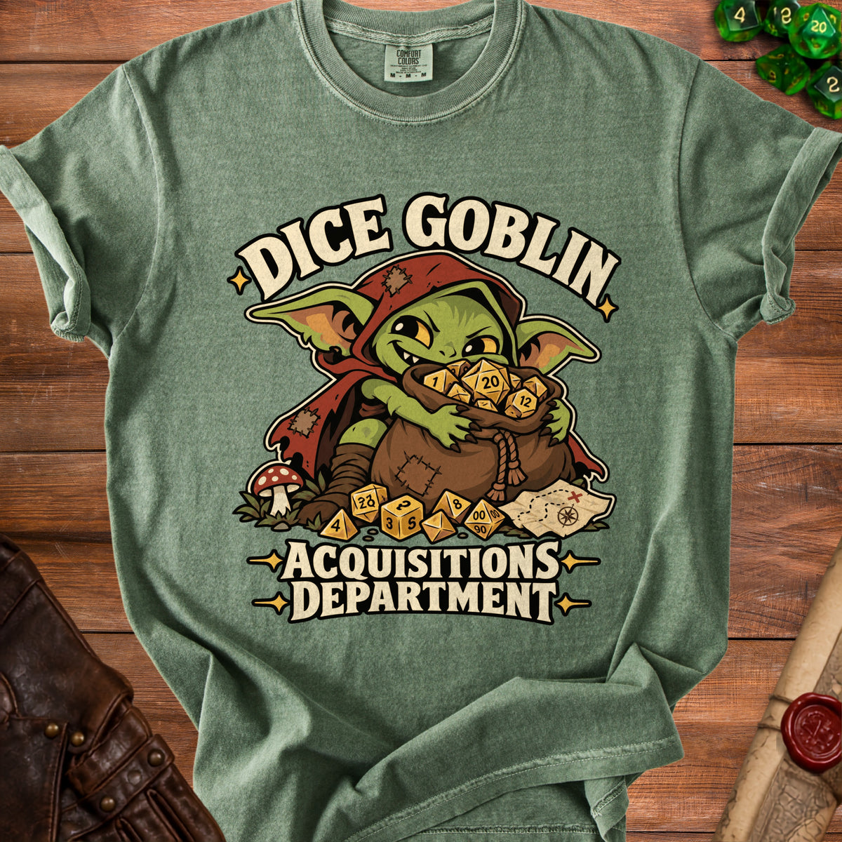 A sage green t-shirt features a graphic of a green goblin hoarding dice, with the text DICE GOBLIN ACQUISITIONS DEPARTMENT.