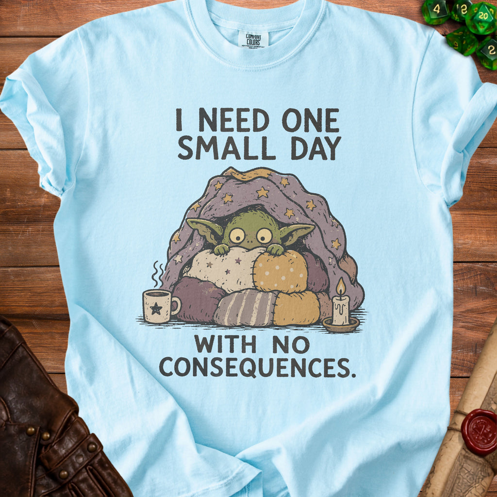 Light blue t-shirt with a goblin under a star-patterned blanket, text says "I NEED ONE SMALL DAY WITH NO CONSEQUENCES."