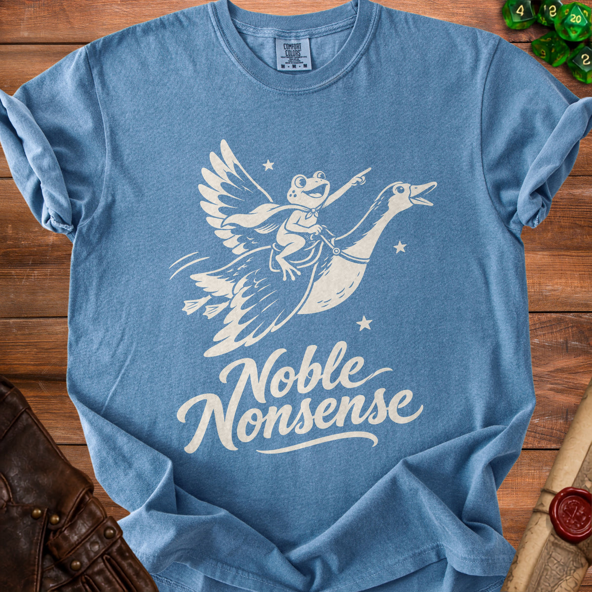 Blue t-shirt featuring a white screen print of a frog riding a flying goose with the text Noble Nonsense.