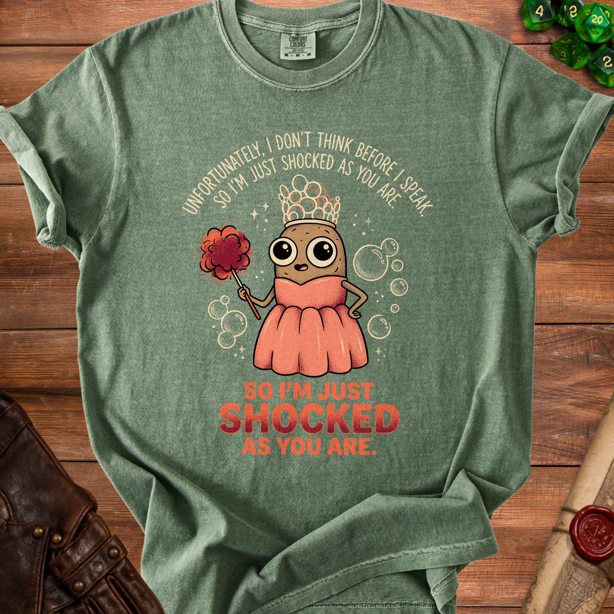 Green t-shirt with cartoon potato wearing crown and pink dress, saying "So I'm just shocked as you are."